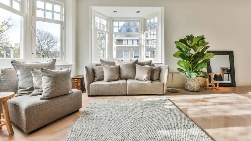Bay-window living room with layered cushions, a textured rug and plants